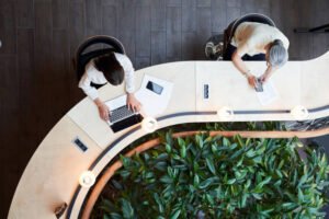Young brunette woman and a senior lady using their devices while sharing a desk and keeping social distance
