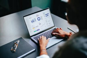 High angle view of an anonymous African-American woman analyzing business graph on a laptop computer while sitting at restaurant desk with notebook and eyeglasses.